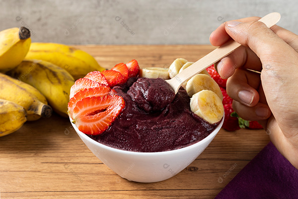 Mão Pegando Açaí na Tigela Sobre uma Mesa de Madeira