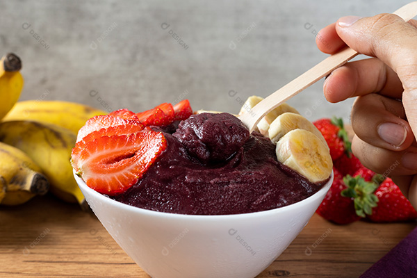 Mão Pegando Açaí na Tigela Sobre uma Mesa de Madeira Vista Frontal