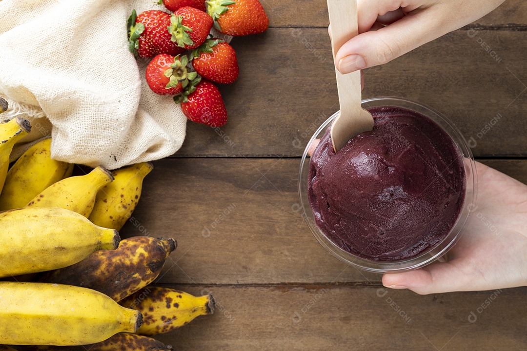 Tigela de Açaí Sendo Segurada por Mãos Sobre Mesa de Madeira