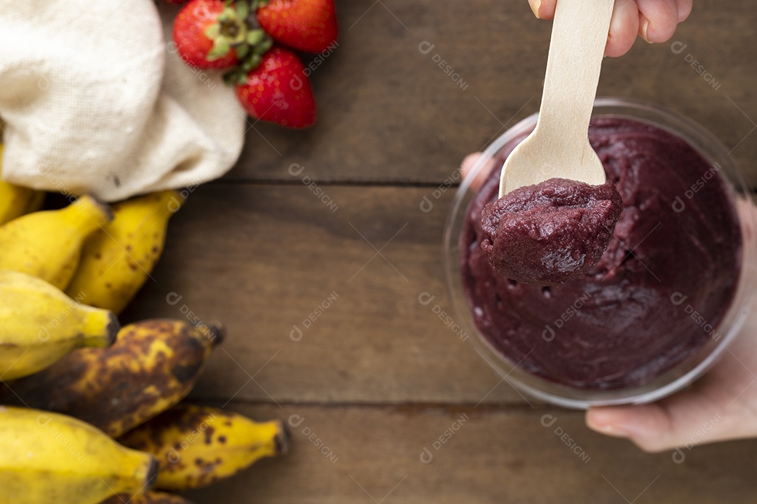 Tigela de Açaí Segurada por Mãos Sobre Mesa de Madeira