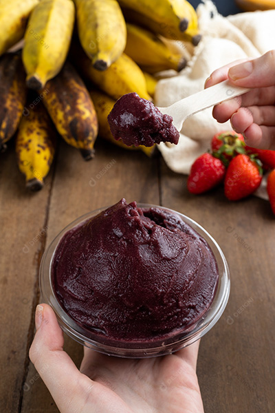 Tigela de Açaí Sendo Segurada por Mãos Sobre Mesa de Madeira