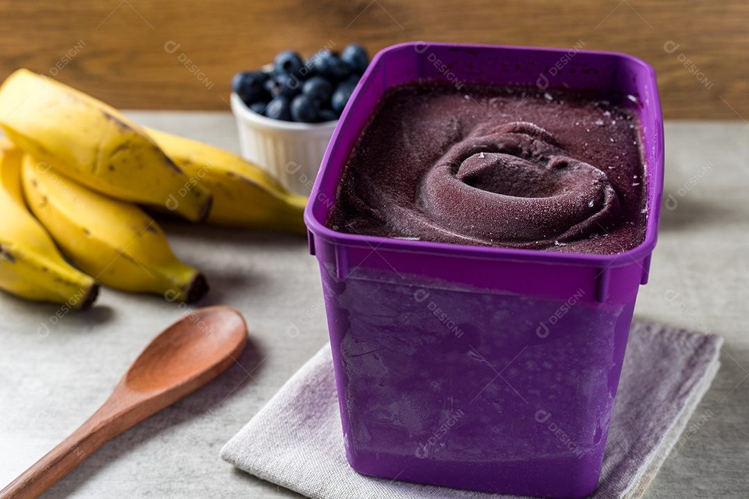 Pote de Sorvete de Açaí Sobre Mesa de Madeira com Frutas ao Fundo