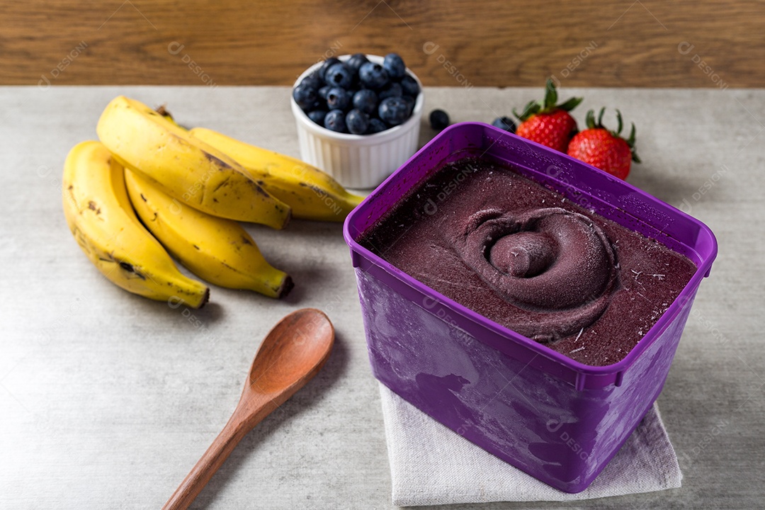 Pote de Sorvete de Açaí Sobre Mesa de Madeira com Frutas ao Fundo Visto de Cima