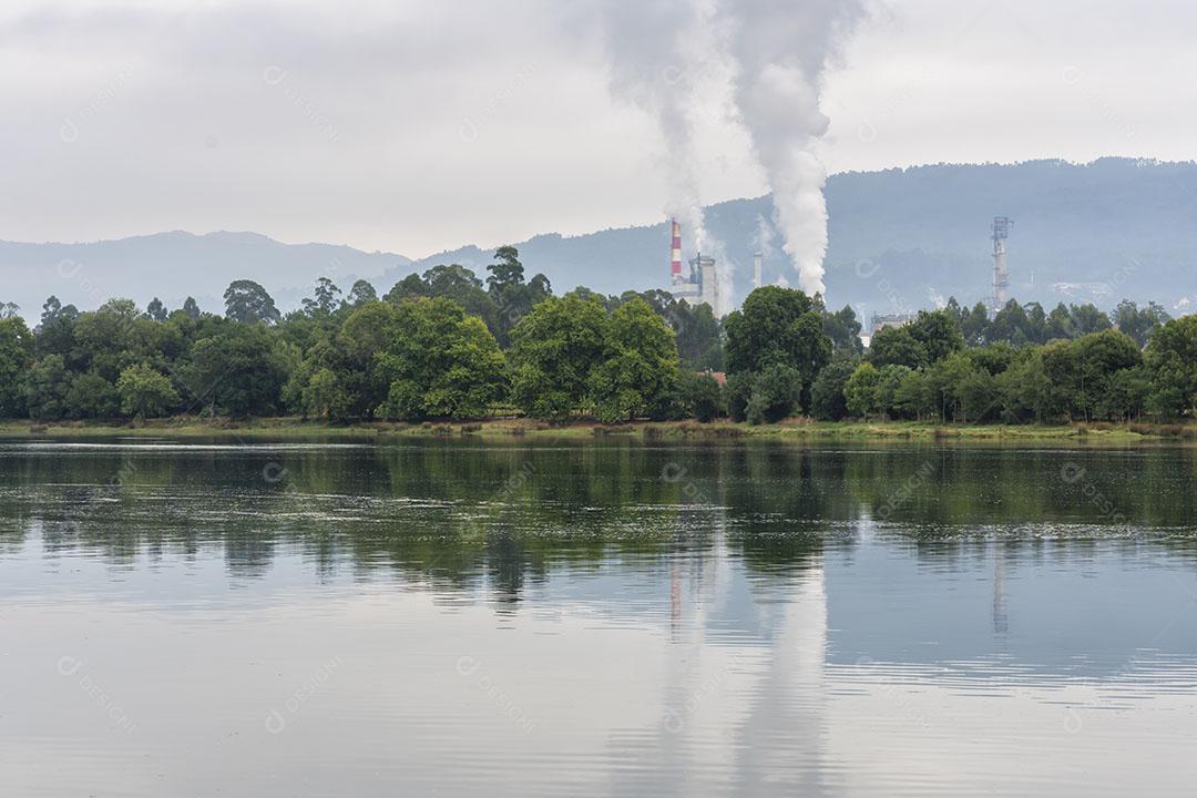Fábrica Com Usina Exalando Fumaça no Meio da Natureza à Beira do Rio Imagem JPG