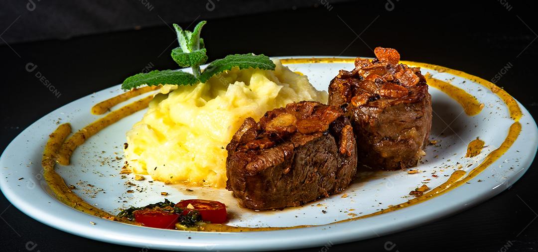 Filé Mignon Com Cebola Frita e Purê De Batata, Decorado Com Tomate Cereja e Molho De Mostarda Em Fundo Preto