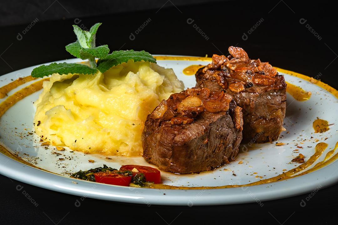 Filé Mignon Com Cebola Frita e Purê De Batata, Decorado Com Tomate Cereja e Molho De Mostarda Em Fundo Preto