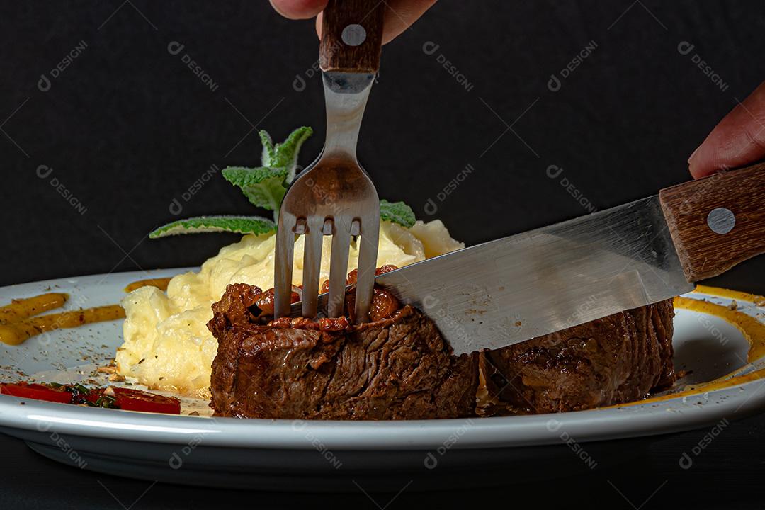 Filé Mignon Com Cebola Frita e Purê De Batata, Decorado Com Tomate Cereja e Molho De Mostarda Em Fundo Preto