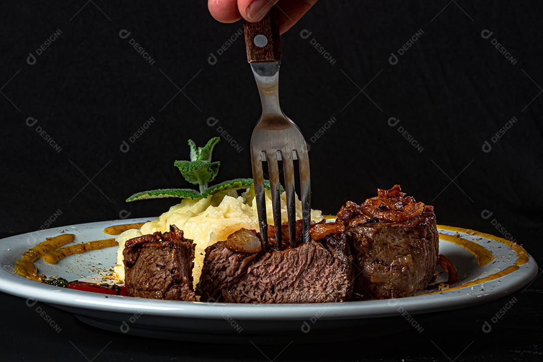 Filé Mignon Com Cebola Frita e Purê De Batata, Decorado Com Tomate Cereja e Molho De Mostarda Em Fundo Preto