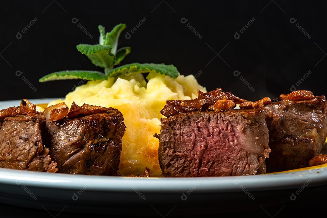 Filé Mignon Com Cebola Frita e Purê De Batata, Decorado Com Tomate Cereja e Molho De Mostarda Em Fundo Preto