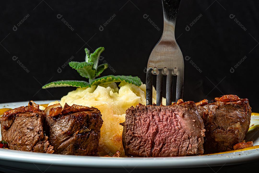 Filé Mignon Com Cebola Frita e Purê De Batata, Decorado Com Tomate Cereja e Molho De Mostarda Em Fundo Preto