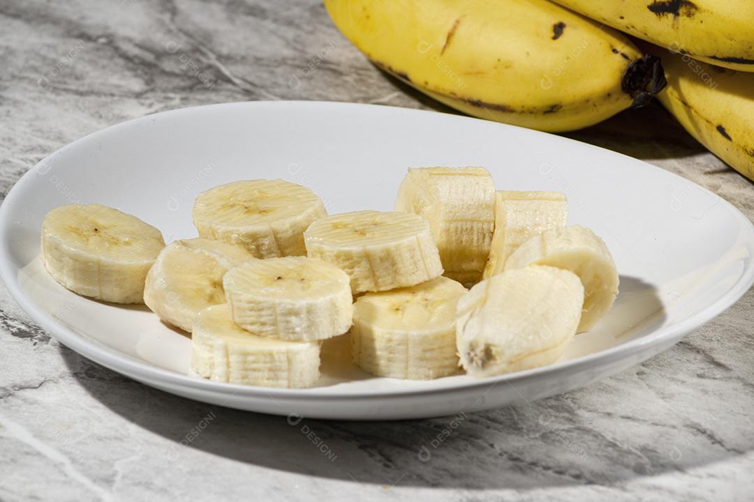 Cacho de Banana e Fatias de Banana Em Um Prato Sobre Uma Mesa Imagem JPG