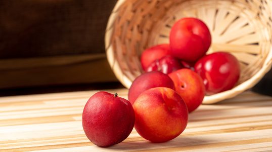 Ameixas Lindas E Suculentas Caidas De Cesta Sobre Mesa De Madeira Imagem JPG