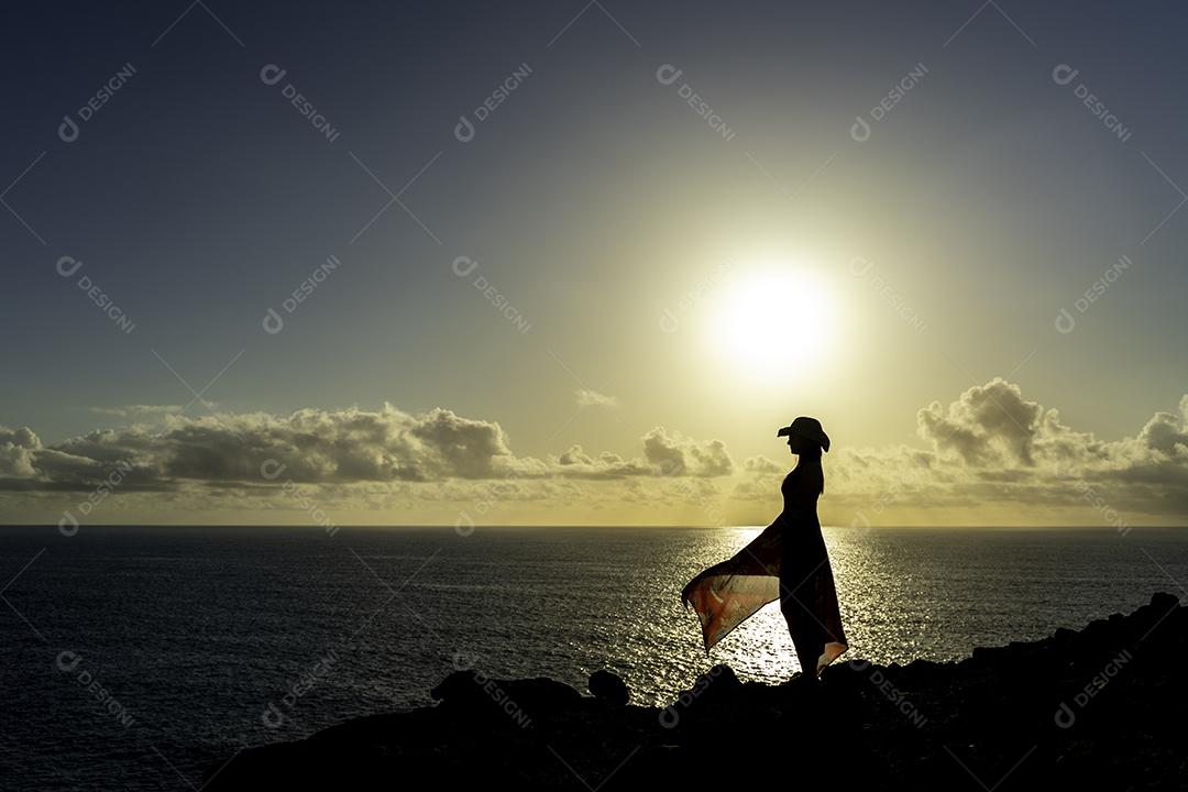 Foto Mulher no Penhasco Perfil Assistindo o Pôr do Sol Vestido Vermelho Transparente