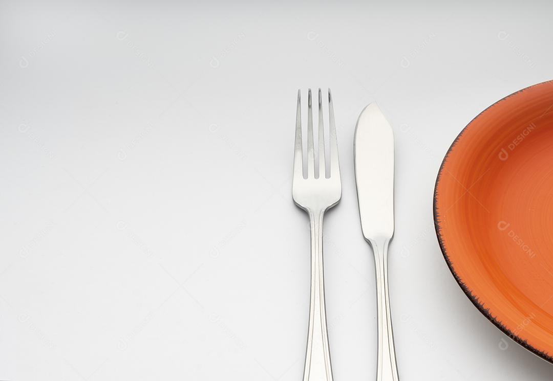 Um Garfo e Uma Faca Ao Lado de Um Prato Laranja na Mesa Imagem JPG