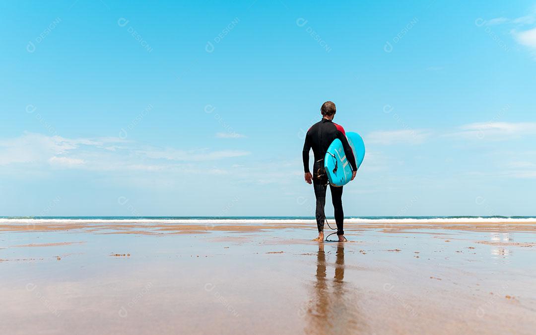 Surfista Na Praia Com Prancha Na Mão Olhando Para  O mar Imagem JPG