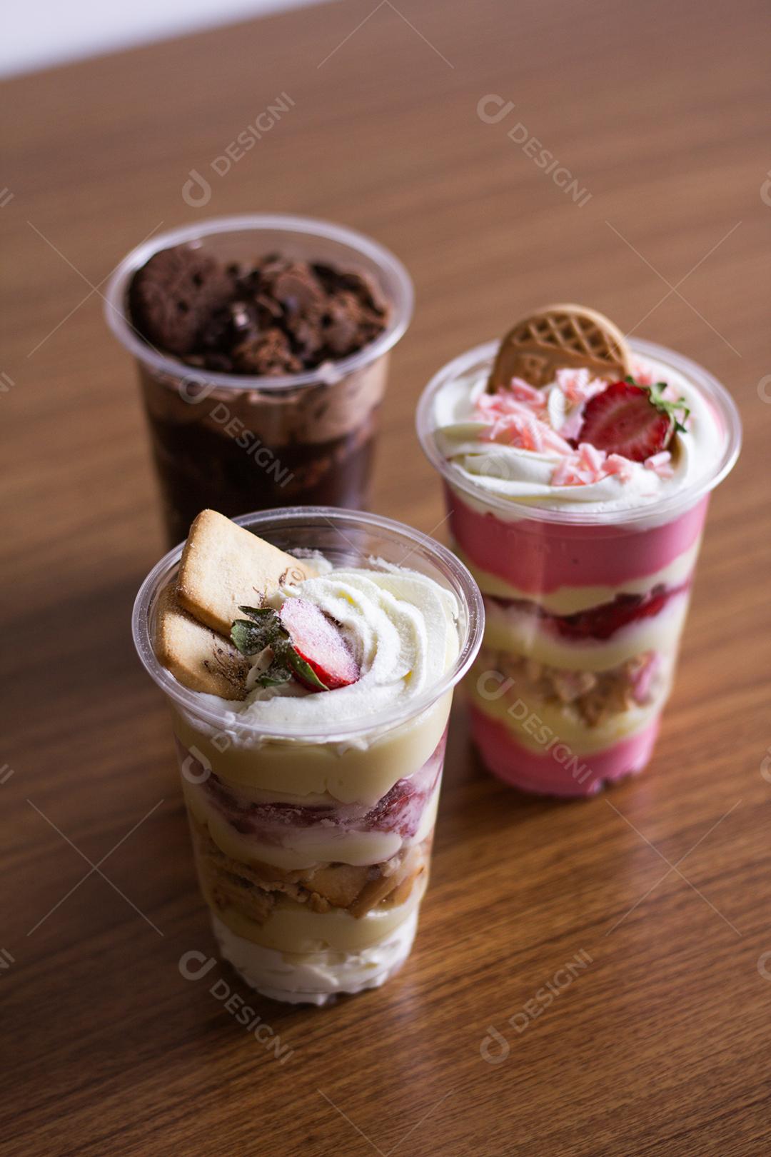 Iogurte servidos em copos de plástico em cima de mesa de madeira