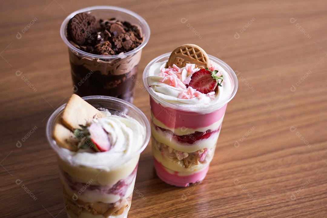 Iogurte servidos em copos de plástico em cima de mesa de madeira