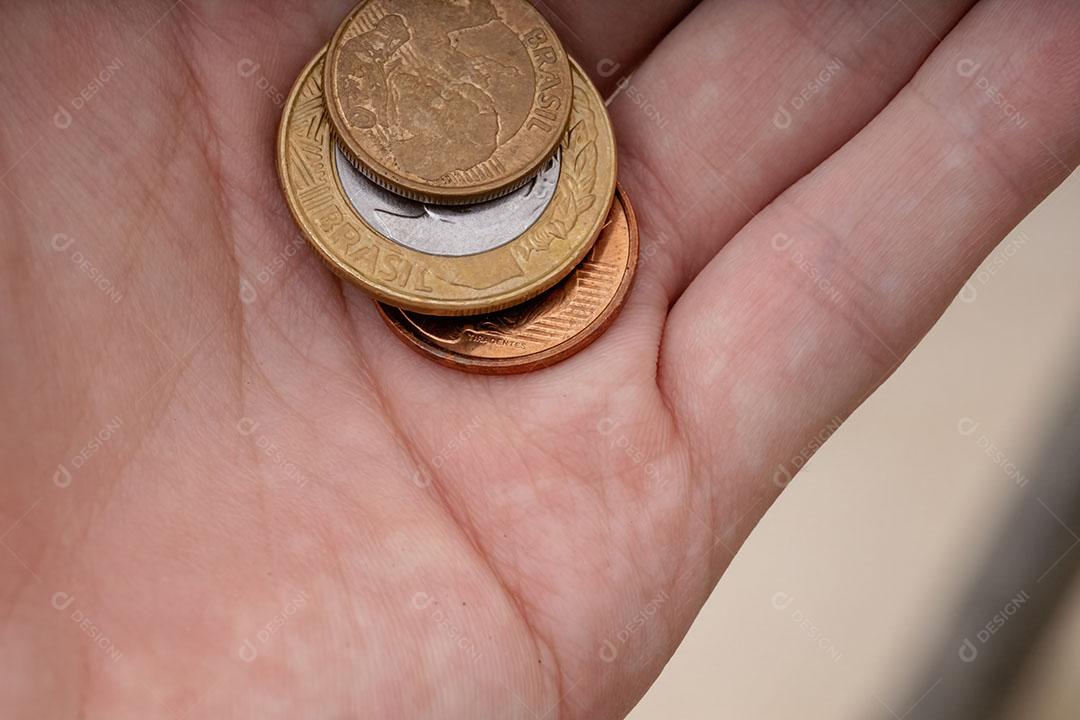 Moedas brasileiras de diferentes valores em uma mão humana