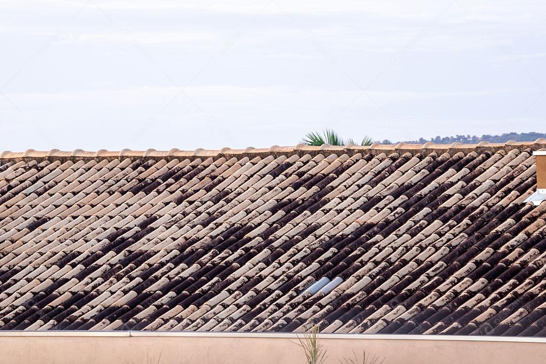 Telhado de residência com telhas escuras e claras e céu azul claro