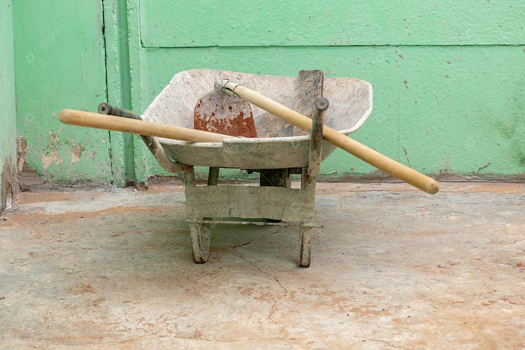Carrinho de mão de metal velho com enxada de cimento sujo