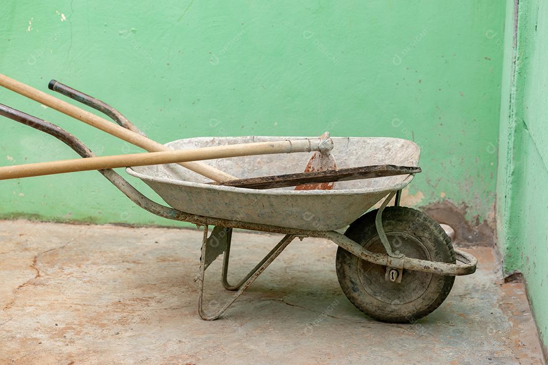 Carrinho de mão de metal velho com enxada de cimento sujo