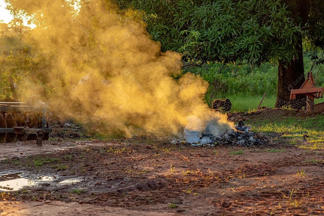Lixo Sendo Queimado em uma Fazenda Gerando Fumaça com Luz Dourada atrás JPG