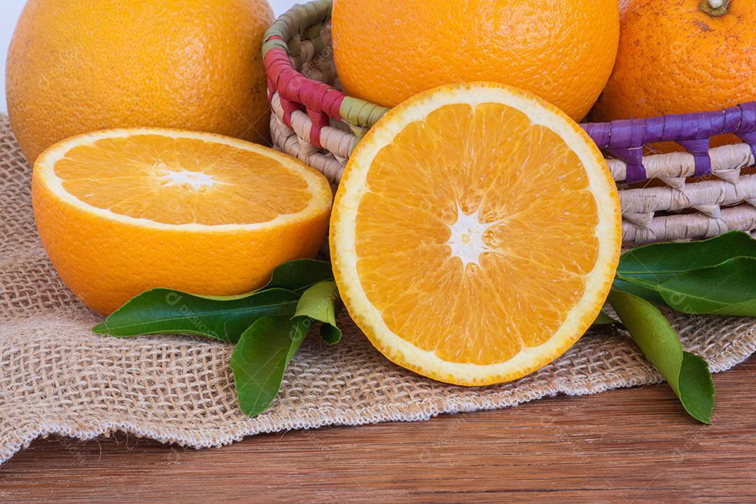 Foto Laranjas Inteiras Maduras e Pedaços Cortados na Cesta na Mesa de Madeira