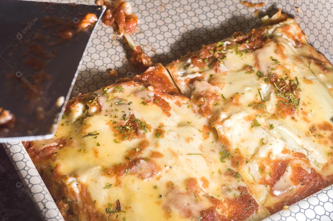 Lasanha em uma panela de alumínio, espátula pegando um pedaço da panela Imagem JPG