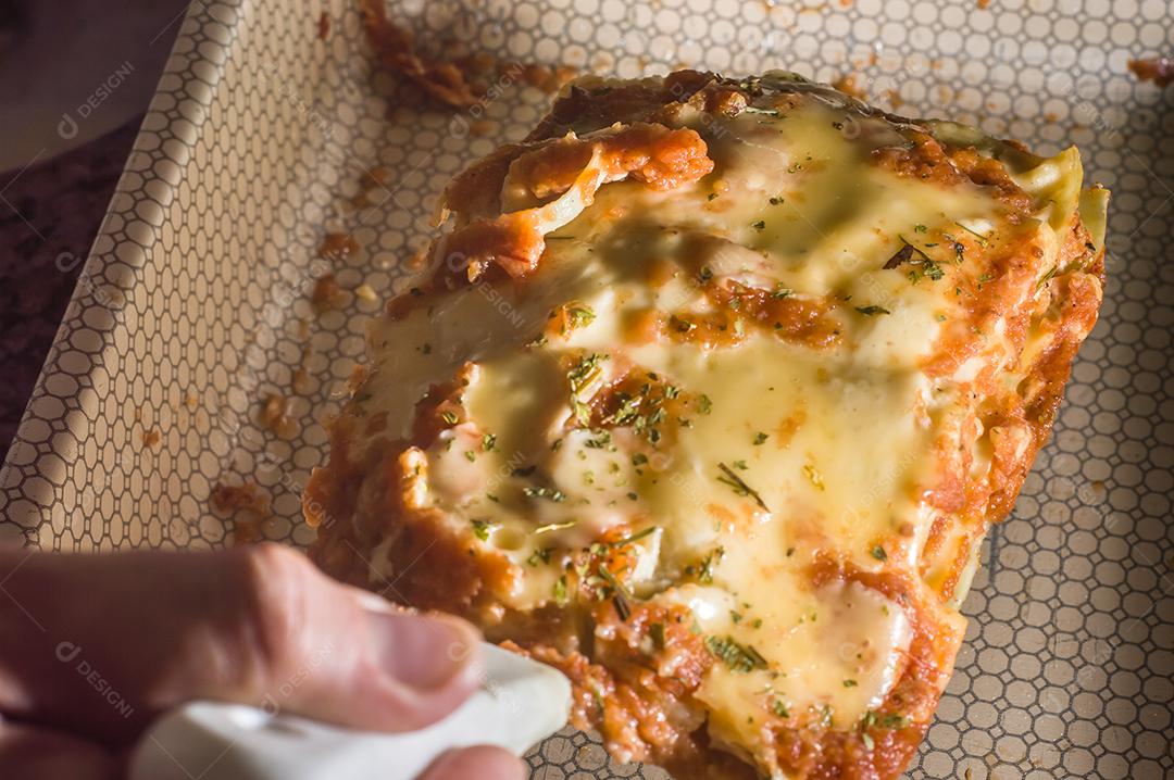 Lasanha em uma panela de alumínio, espátula pegando um pedaço da panela Imagem JPG