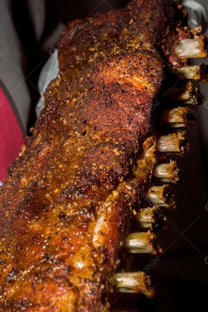 Costela bovina defumada com fundo escuro homem segurando a costela, churrasco