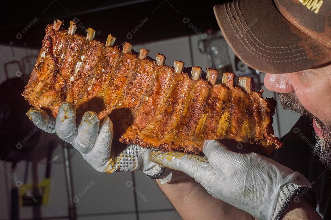 Costela bovina defumada com fundo escuro homem segurando a costela, churrasco