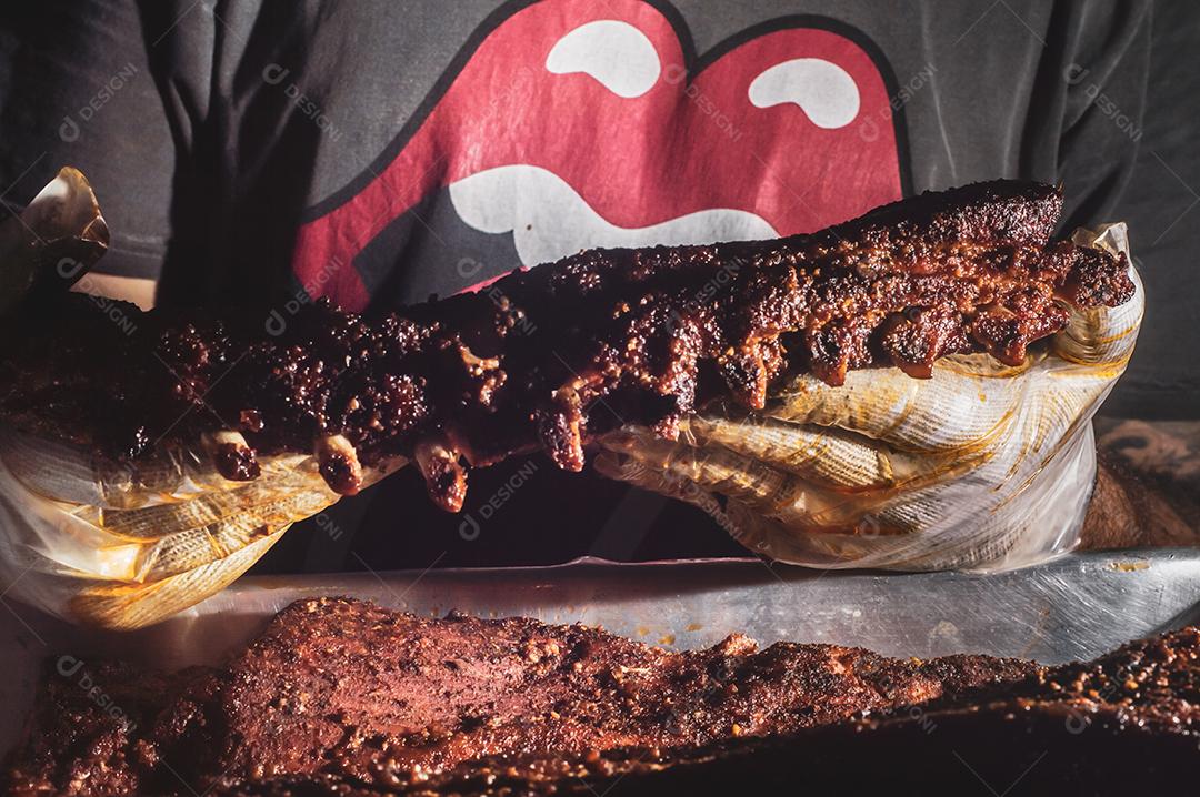 Costela bovina defumada com fundo escuro homem segurando a costela, churrasco