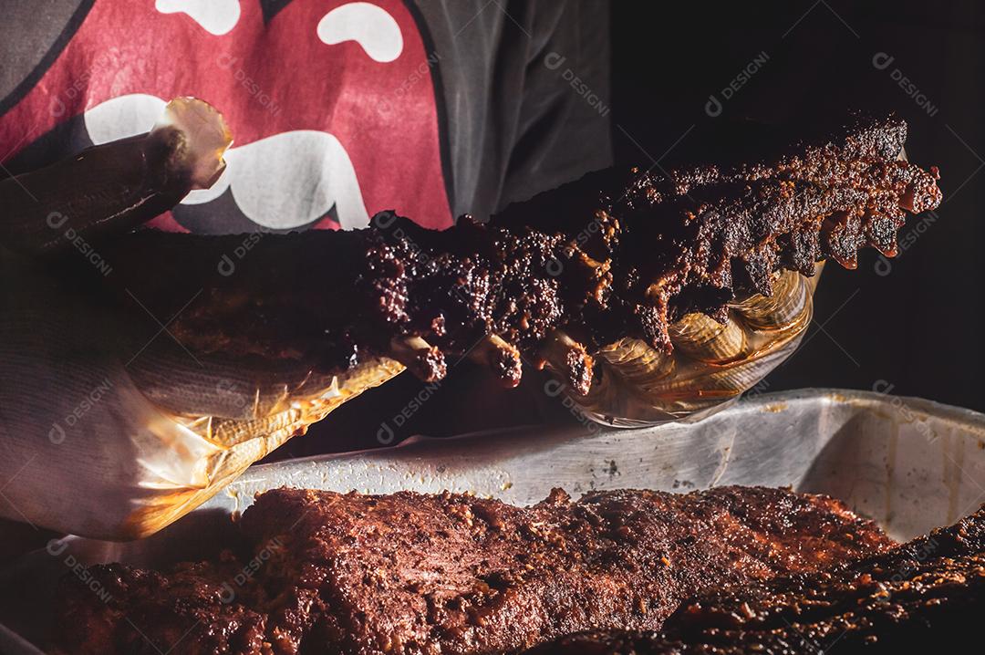 Costela bovina defumada com fundo escuro homem segurando a costela, churrasco