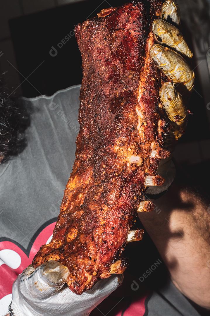 Costela bovina defumada com fundo escuro homem segurando a costela, churrasco