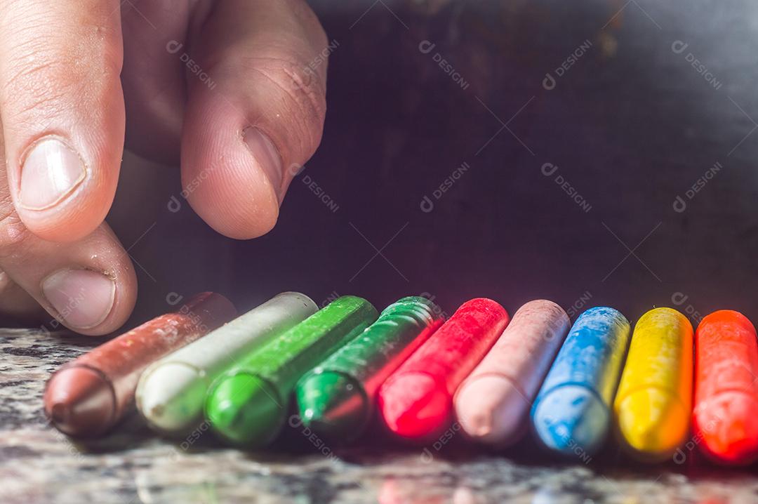 Diversidade de cores focadas em giz de cera e homens desfocados ao fundo em uma porta