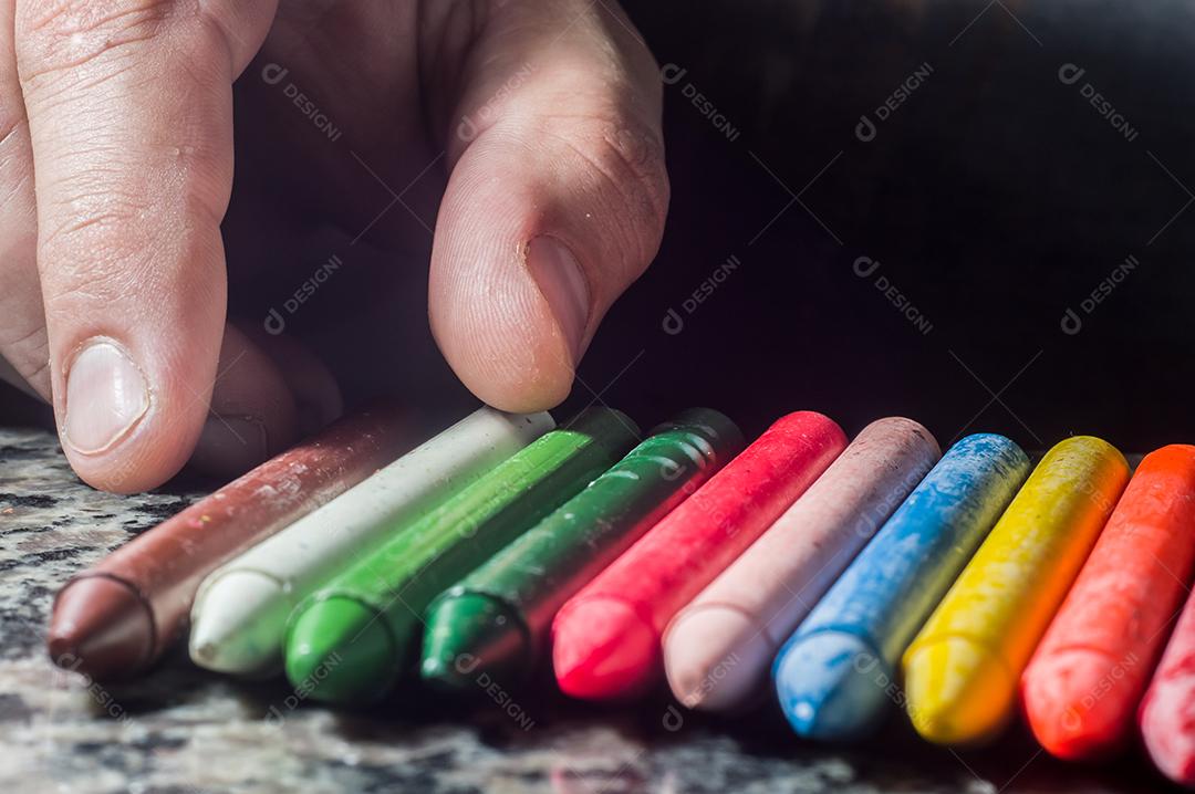Diversidade de cores focadas em giz de cera e homens desfocados ao fundo em uma porta