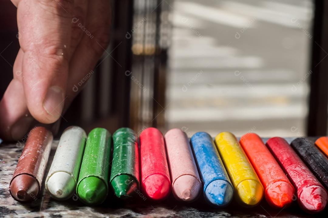 Diversidade de cores focadas em giz de cera e homens desfocados ao fundo em uma porta
