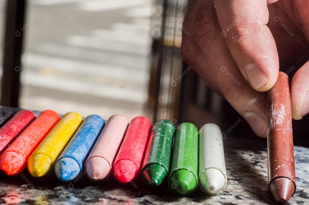 Diversidade de cores focadas em giz de cera e homens desfocados ao fundo em uma porta
