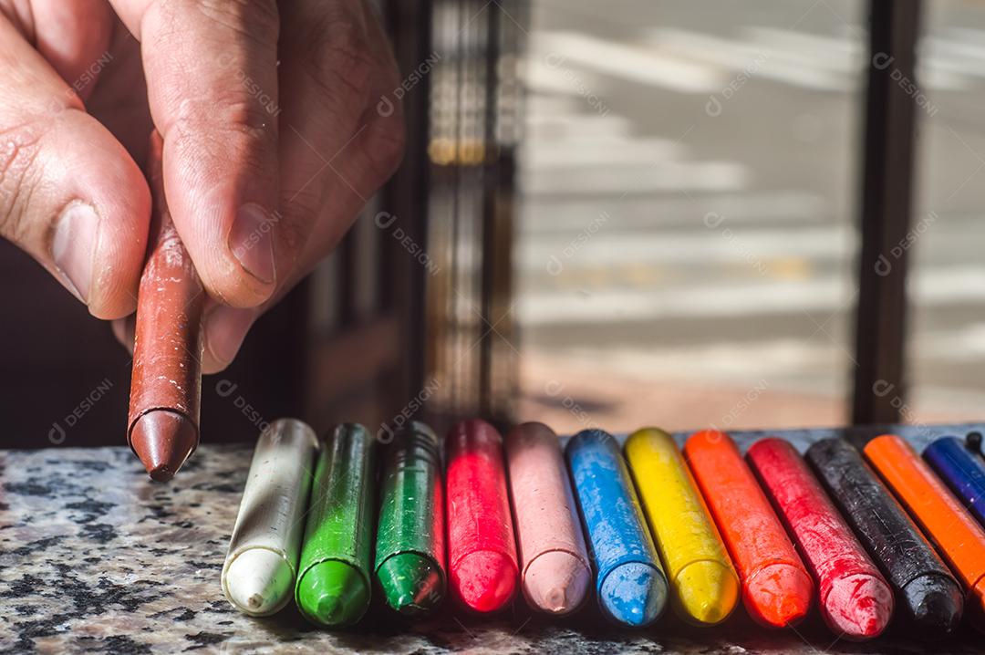 Diversidade de cores focadas em giz de cera e homens desfocados ao fundo em uma porta