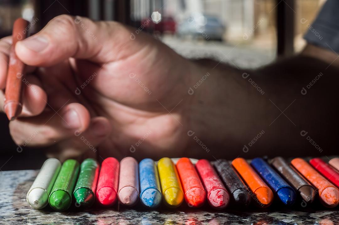 Diversidade de cores focadas em giz de cera e homens desfocados ao fundo em uma porta