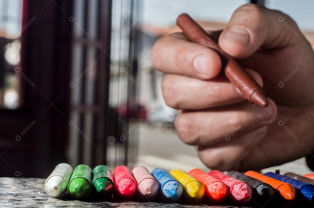 Diversidade de cores focadas em giz de cera e homens desfocados ao fundo em uma porta