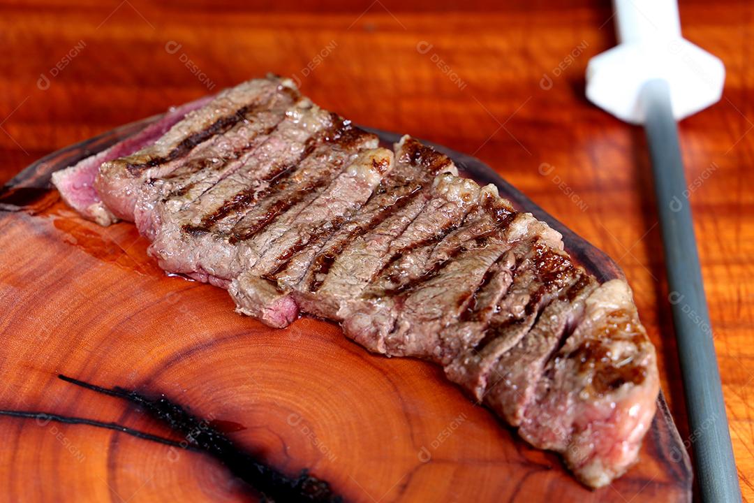 Picanha ou Bife de Alcatra. Cortando um bife suculento em uma placa de madeira JPG