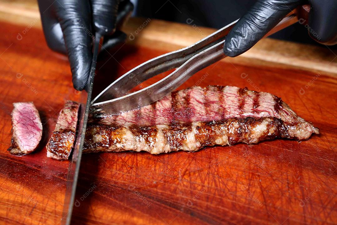 Picanha ou Bife de Alcatra. Cortando um bife suculento em uma placa de madeira JPG