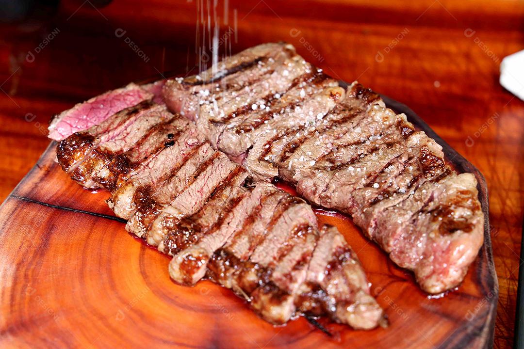 Picanha ou Bife de Alcatra. Cortando um bife suculento em uma placa de madeira JPG