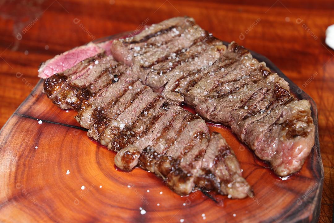 Picanha ou Bife de Alcatra. Cortando um bife suculento em uma placa de madeira JPG