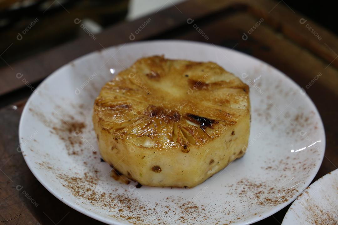 Abacaxi grelhado no churrasco, com marcas de grelha e canela por cima. em uma placa branca JPG