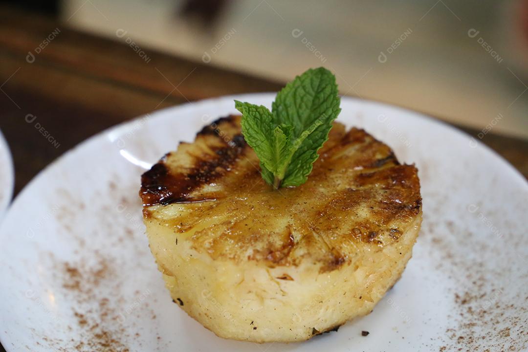 Abacaxi grelhado no churrasco, com marcas de grelha e canela por cima. em uma placa branca JPG