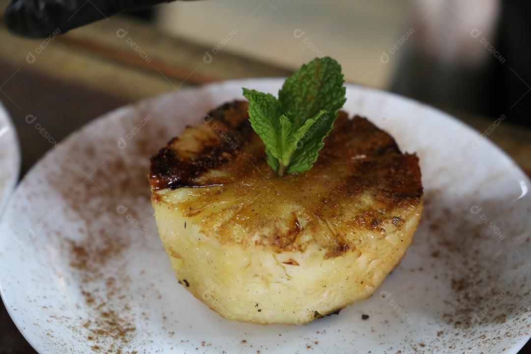 Abacaxi grelhado no churrasco, com marcas de grelha e canela por cima. em uma placa branca JPG