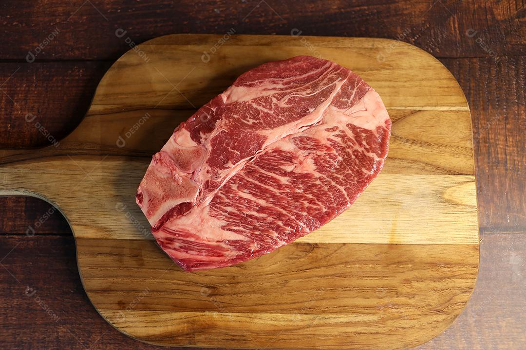 Costela Curta ou Costela Premium. Belo bife cru sob uma tábua de madeira em um fundo de madeira. Para um churrasco brasileiro JPG