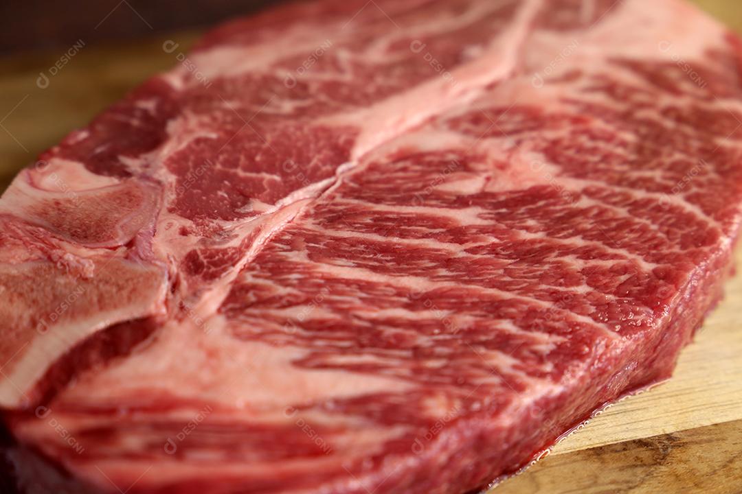 Costela Curta ou Costela Premium. Belo bife cru sob uma tábua de madeira em um fundo de madeira. Para um churrasco brasileiro JPG